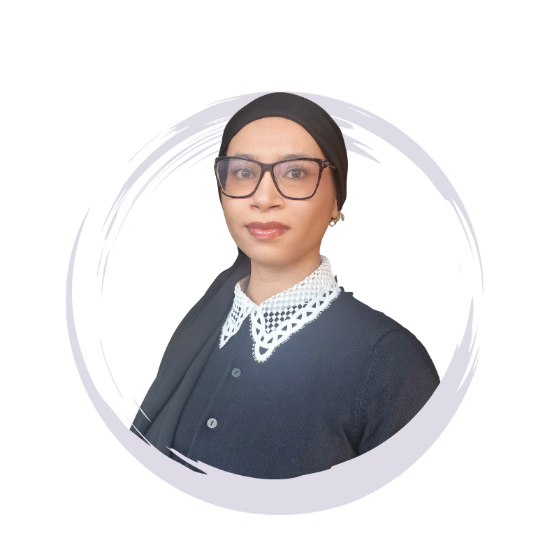 A woman wearing a black headscarf, black glasses, a black shirt, and a white lacy collar, standing against a plain background.
