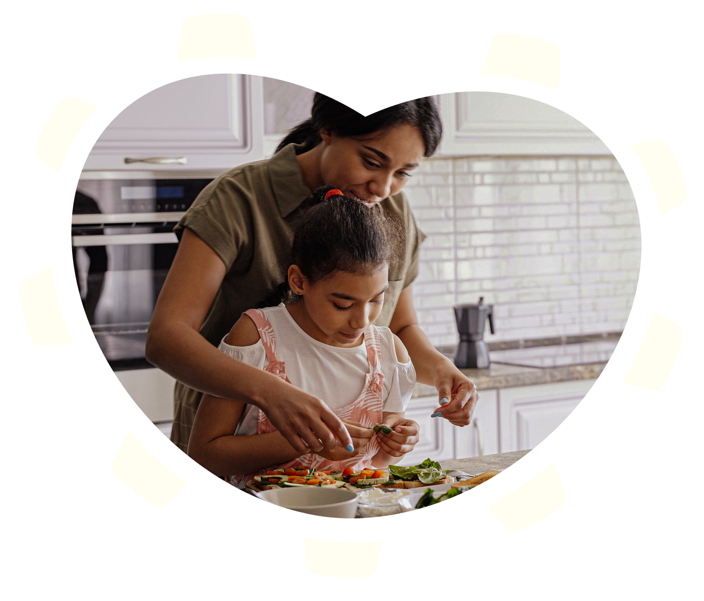 A woman and young girl preparing food together in a kitchen, with vegetables and greens on the counter.