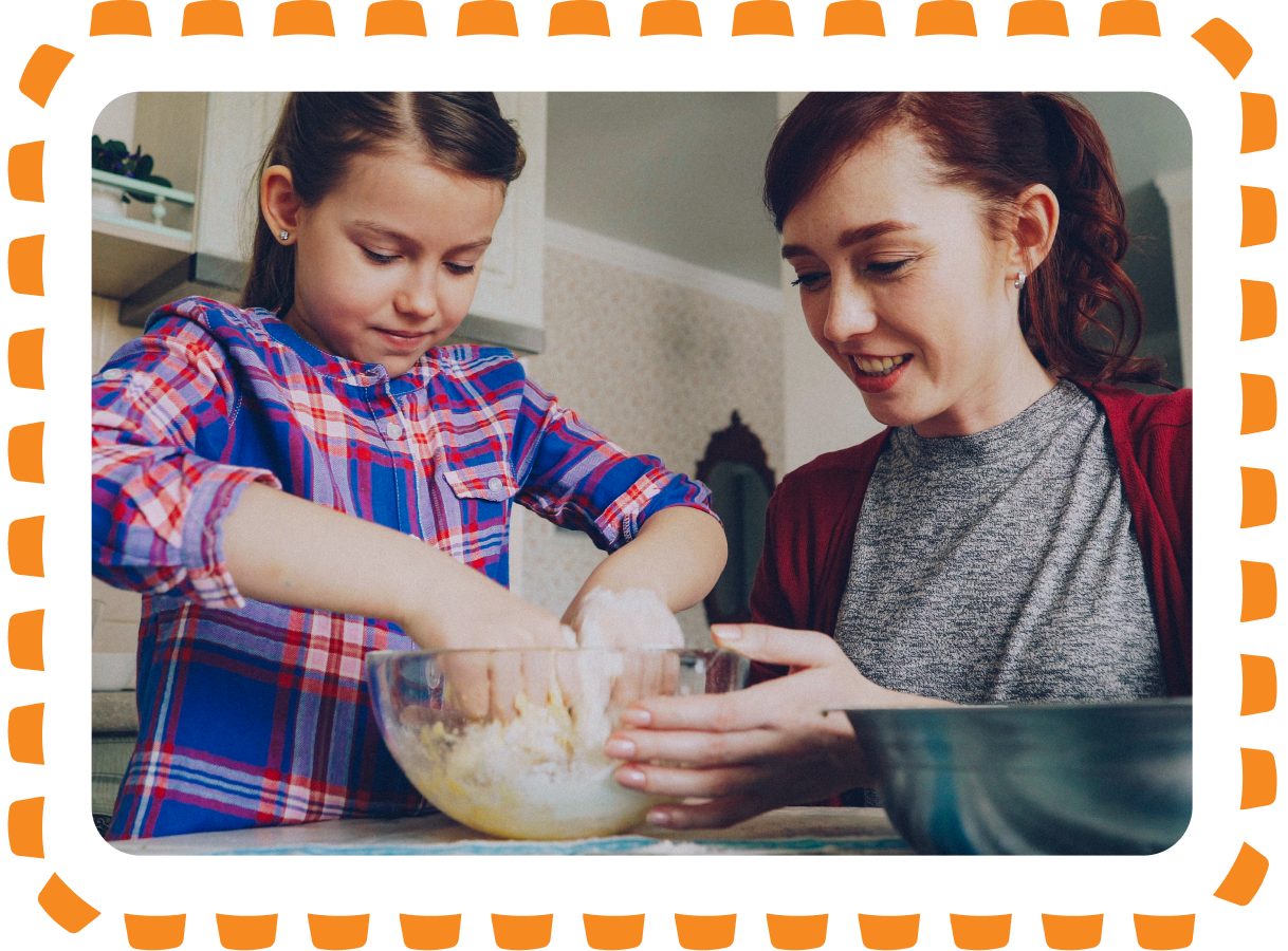 A woman and a girl baking together in a kitchen, mixing ingredients in a glass bowl.