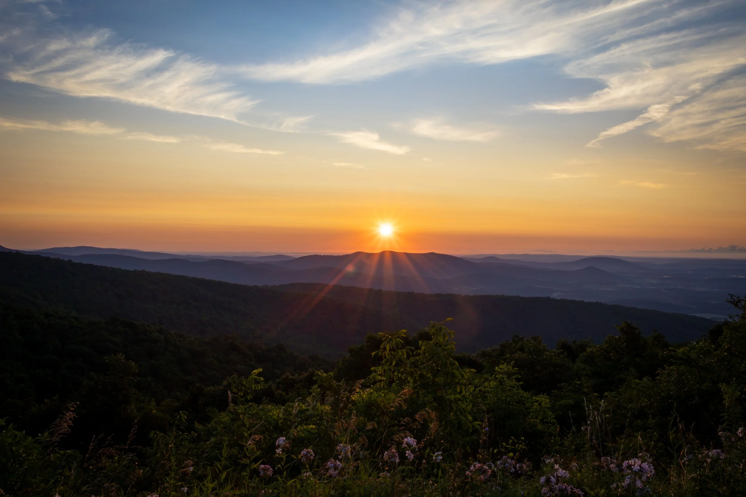 Sunset over rolling hills with scattered clouds in the sky.