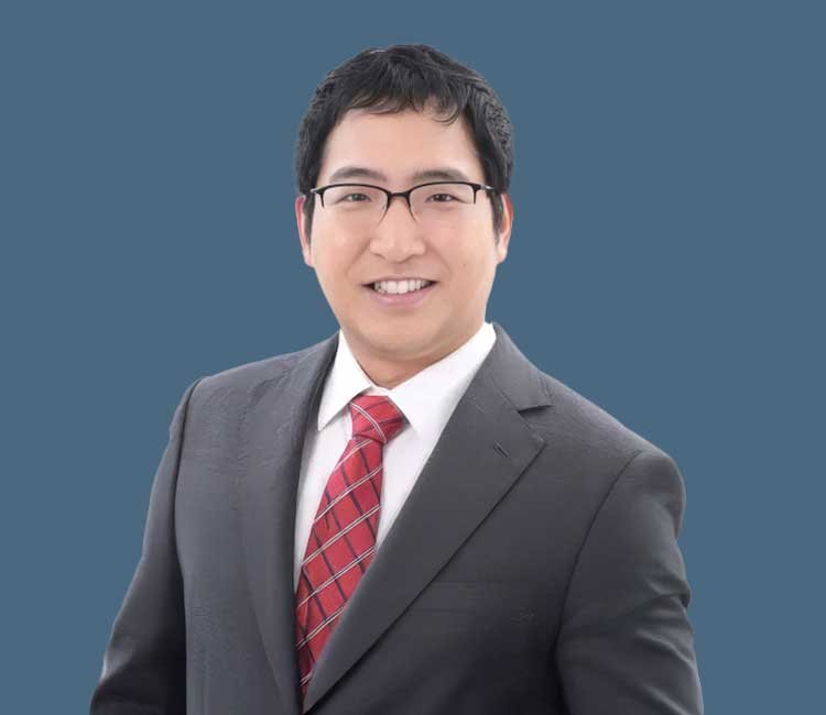 Professional portrait of a man in a suit and glasses against a solid blue background.