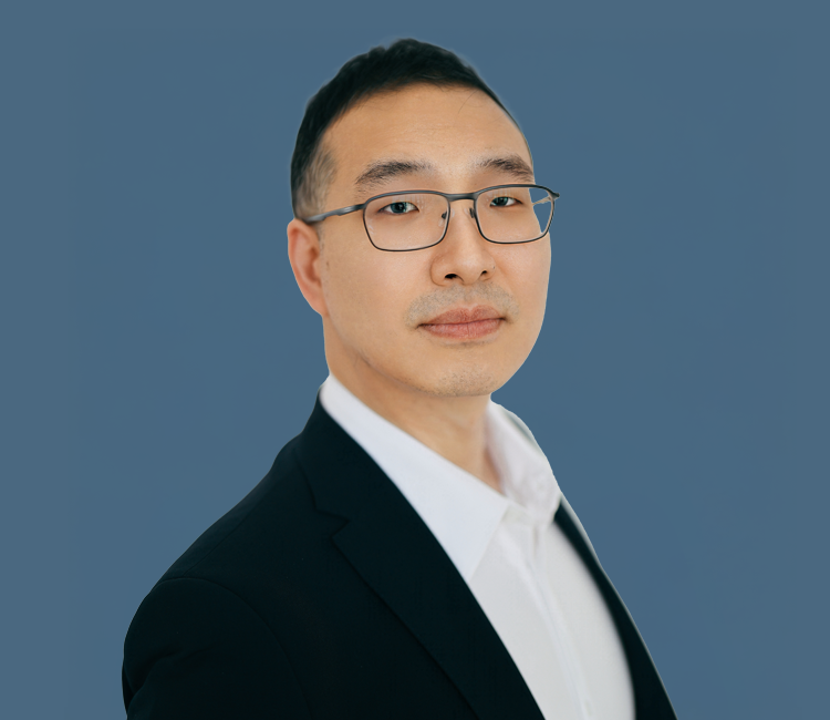 Portrait of a man in a suit with glasses against a blue background.