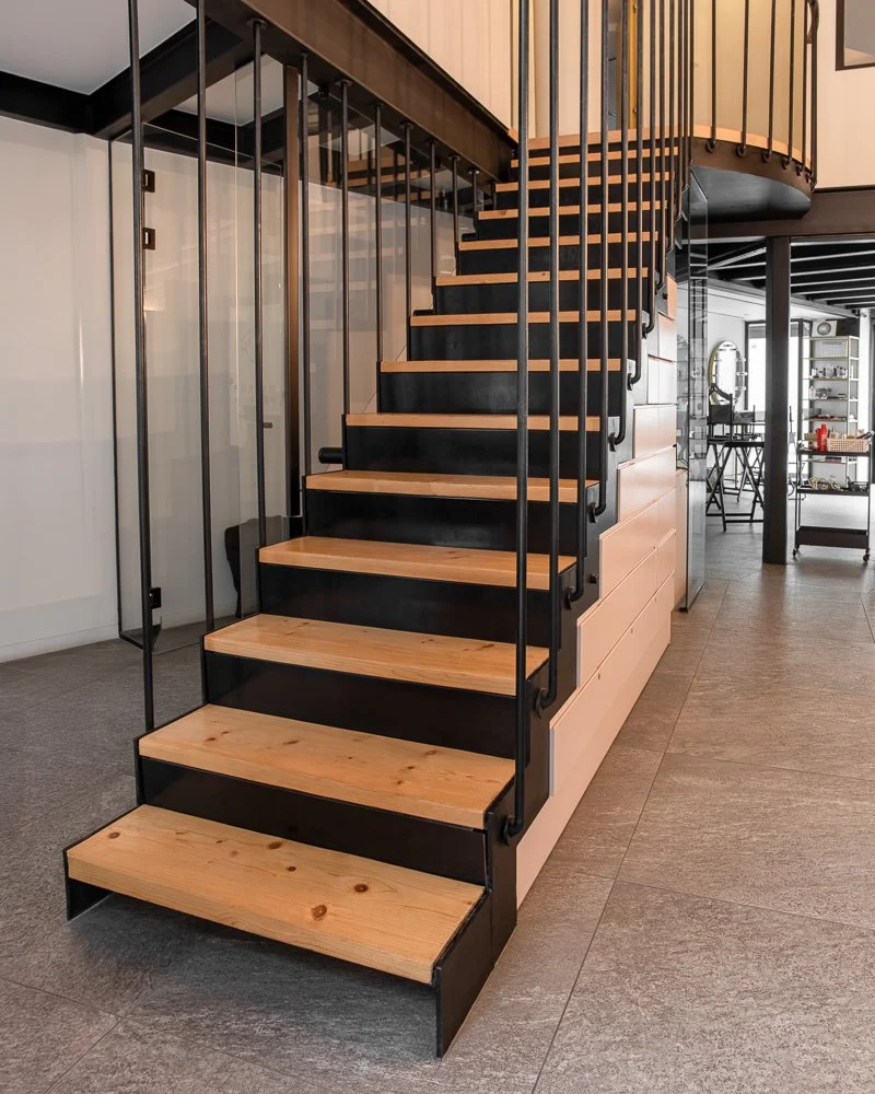 Modern indoor staircase with wooden treads and black metal frame, leading to a second floor in a contemporary home.