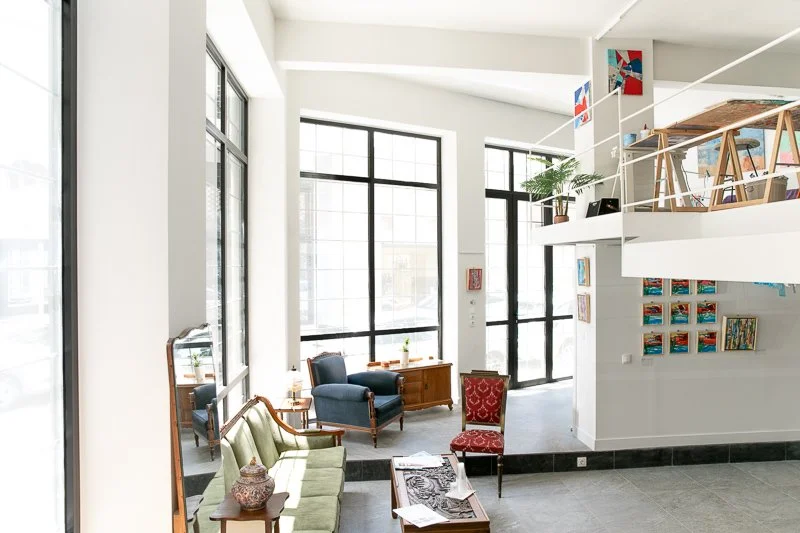 Bright, modern lobby or lounge area with large windows, colorful artwork, and a mix of vintage and contemporary furniture.