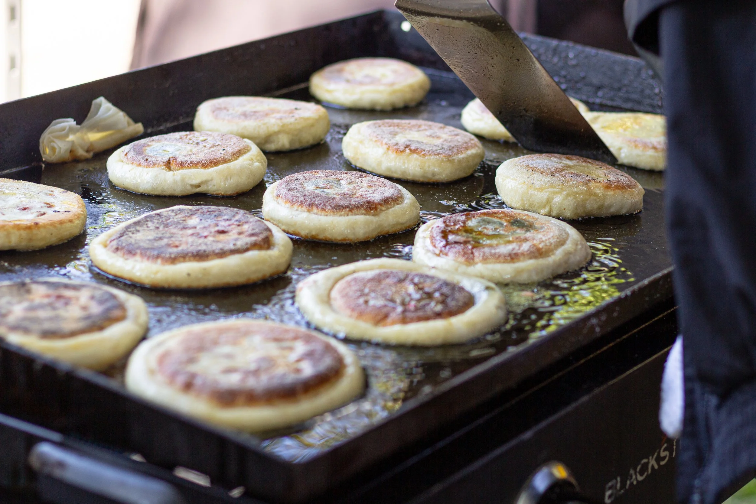 Hotteok (Korean filled pancakes) cooking on an electric griddle with a spatula flipping one of them.