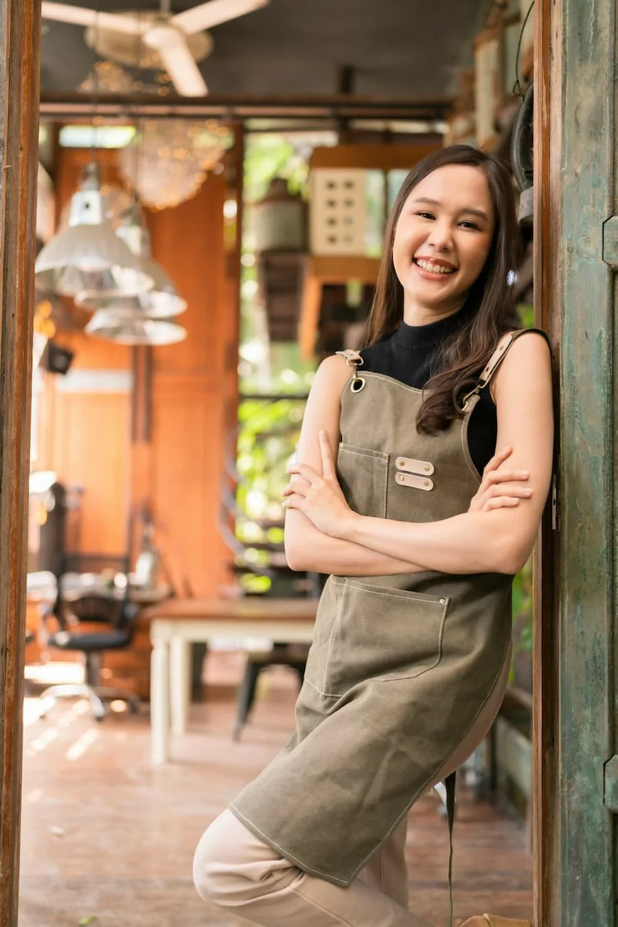 A woman with long dark hair smiling with arms crossed, standing inside a rustic wooden room.