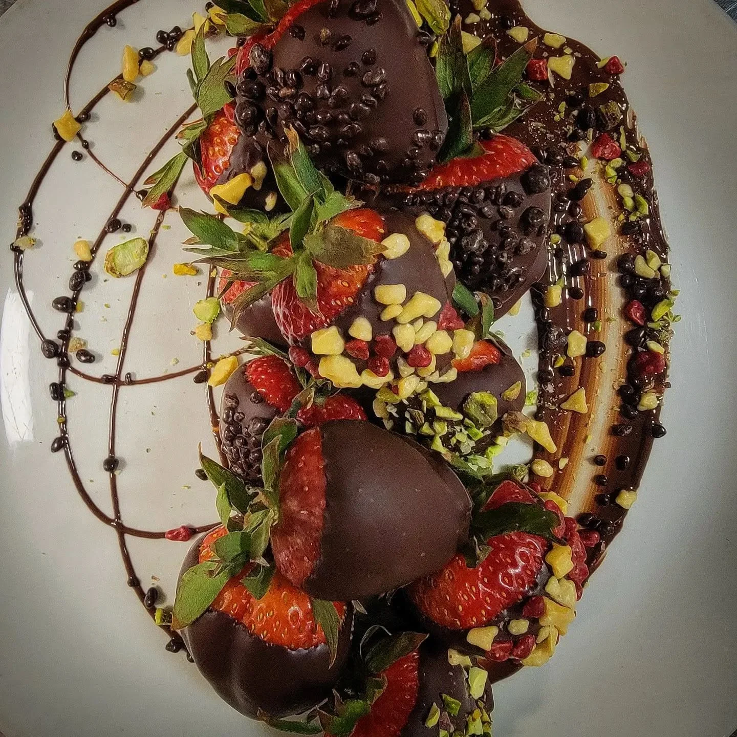 A dessert decorated with strawberries, chocolate-covered strawberries, chopped nuts, and chocolate drizzle, arranged on a white plate.