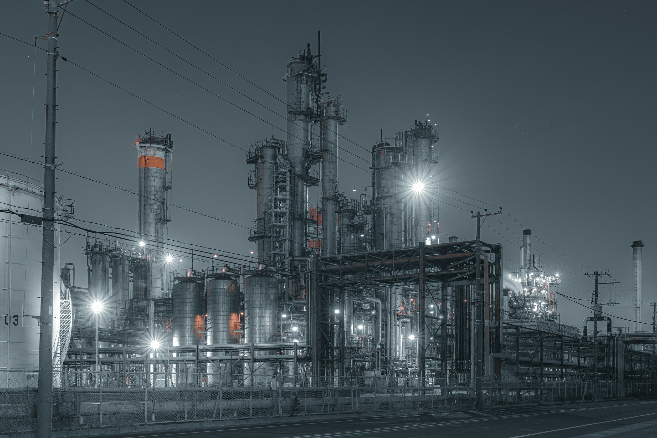 Industrial factory complex at night with steel structures, pipes, and bright lights.