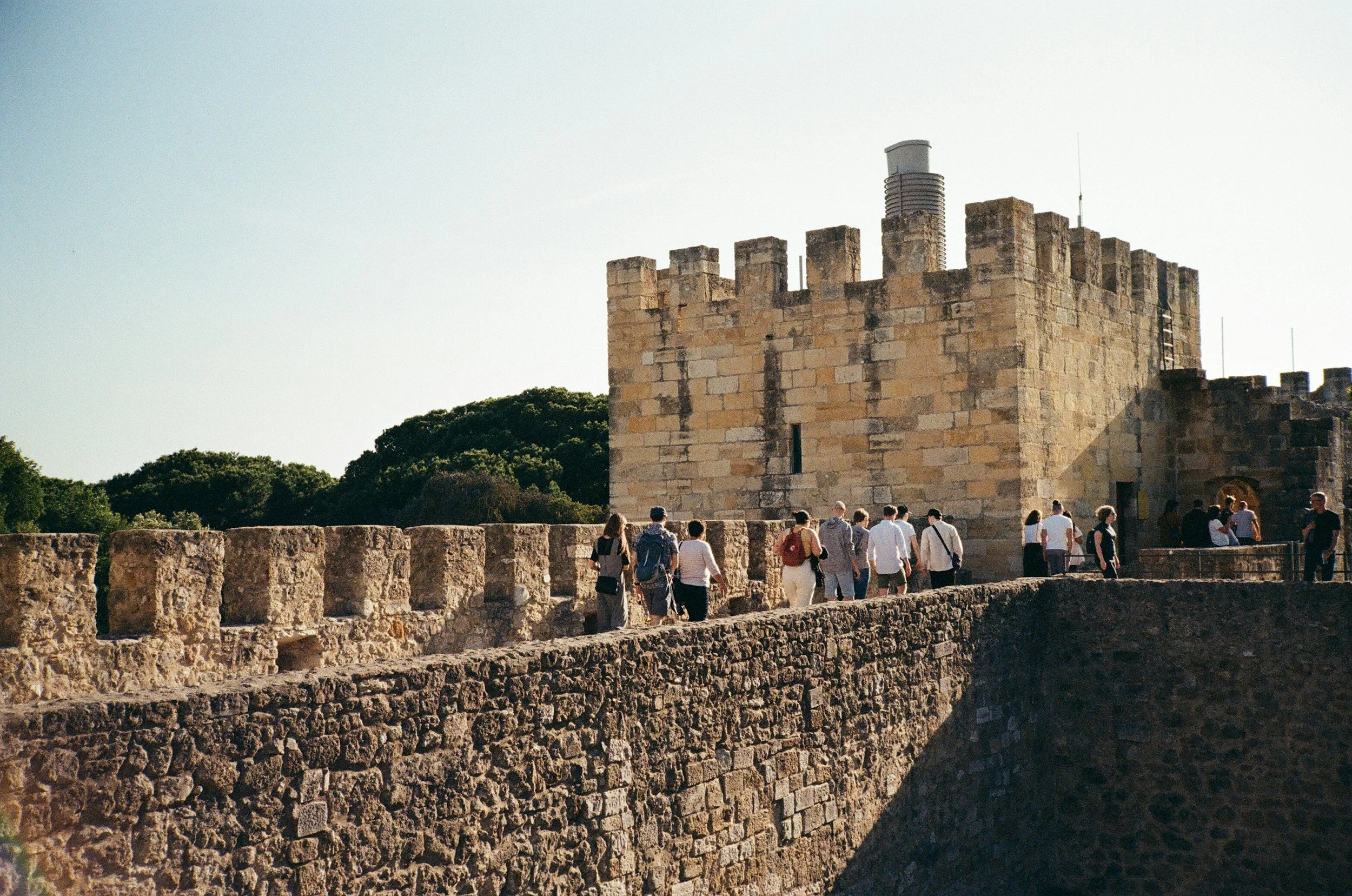 An old fortress souranded by trees and with people walking accorss it