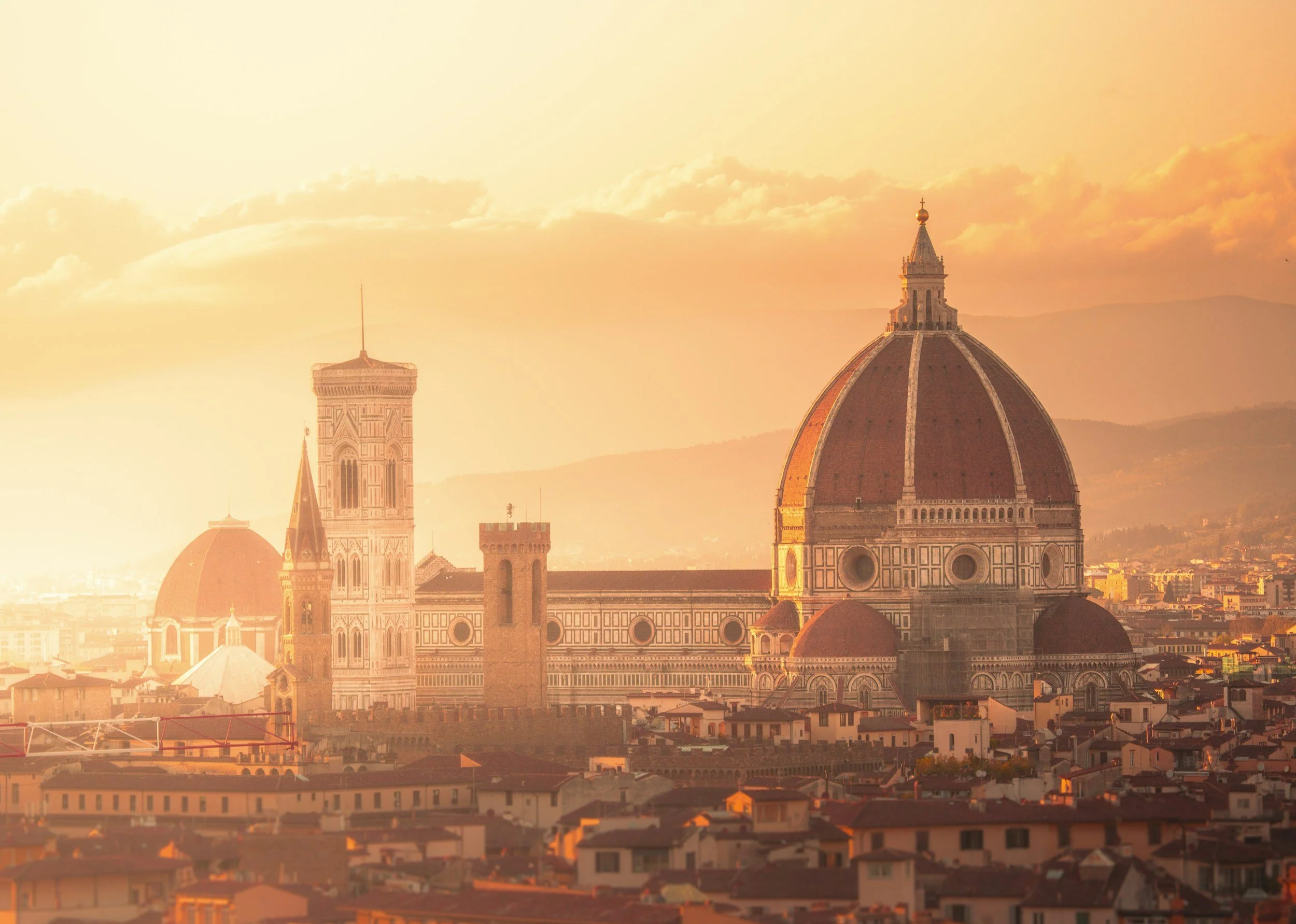 Sunset over Florence, Italy, showcasing the Florence Cathedral's dome and the Palazzo Vecchio tower, with warm golden and orange hues illuminating the city skyline.