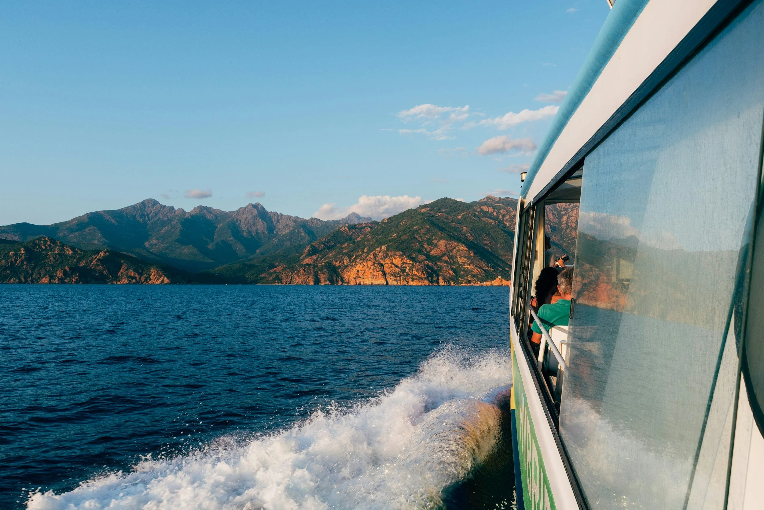 The image shows a boat speeding across a large body of water with mountains in the background. The sky is partly cloudy, and the boat has a reflection on the water's surface.