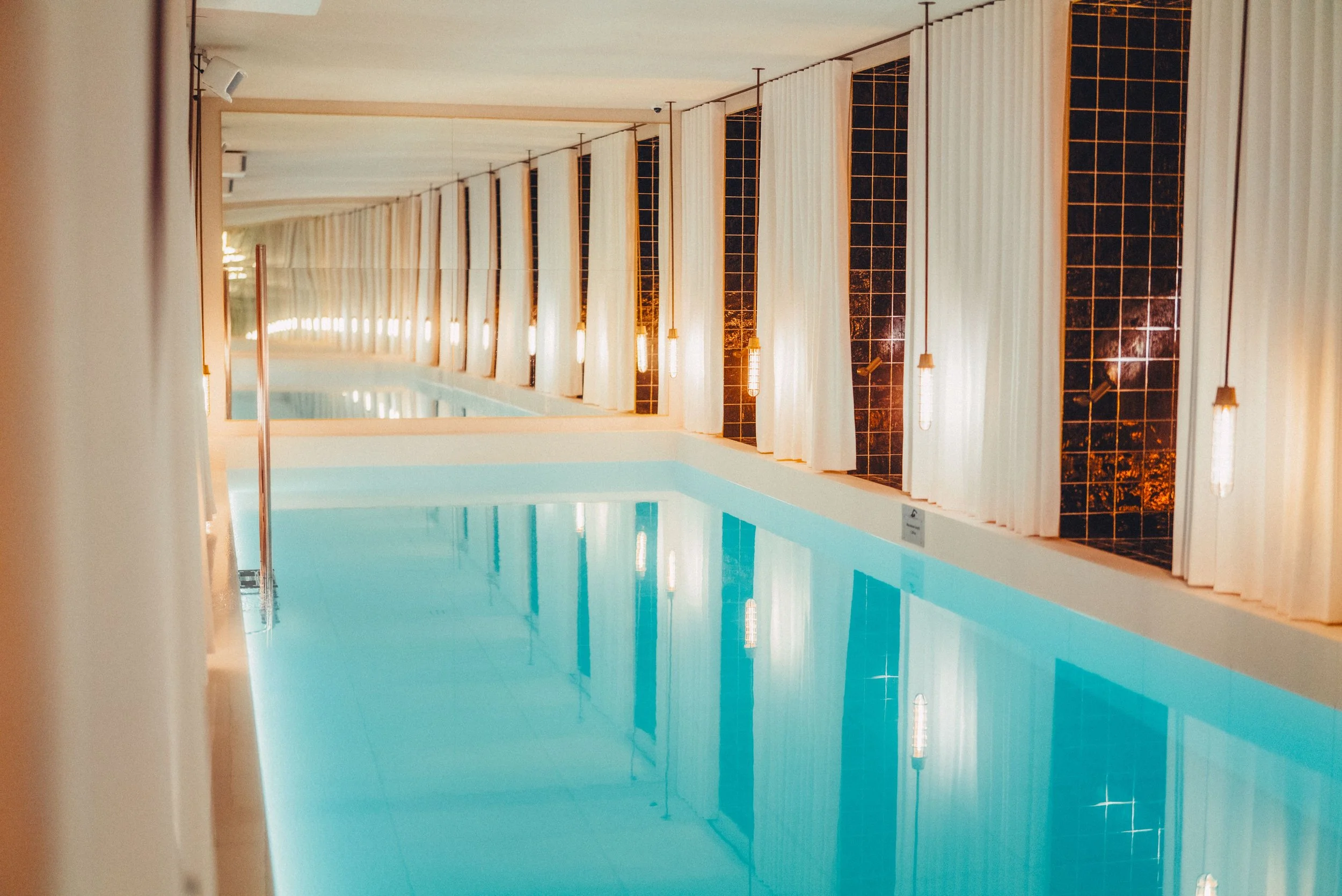 Indoor swiming pool at hotel Brach Madrid. On the walls there are white curtians and golden tiles.
