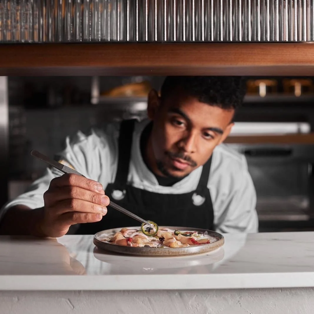 Chef placing toppings on a pizza in a kitchen.