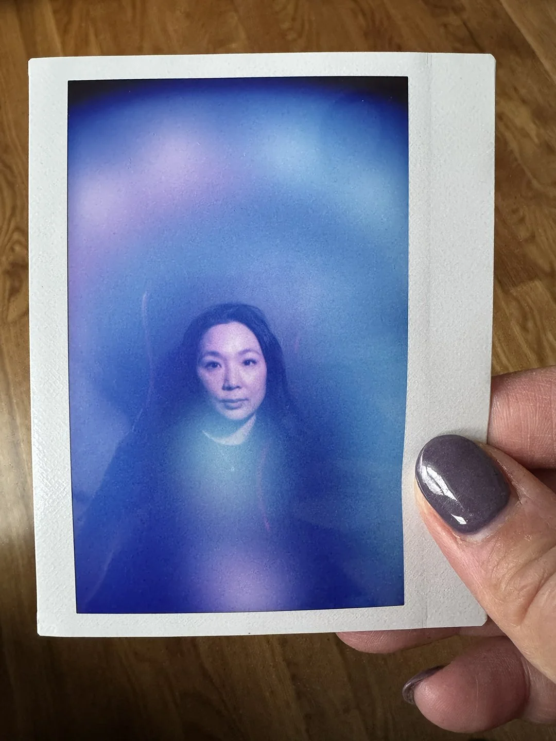 A woman holding a Polaroid photo of herself with a colorful, blurred background.