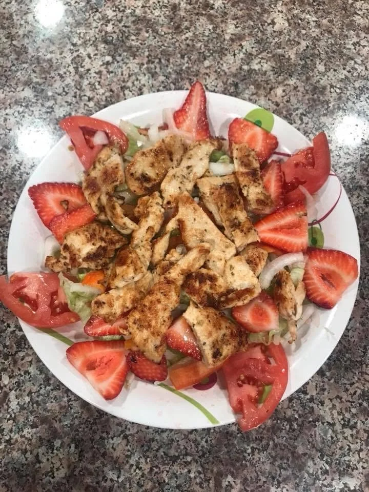 Plate with grilled chicken strips, strawberries, tomatoes, and onions on a countertop.