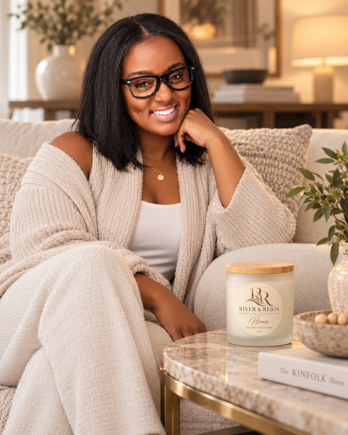 A woman relaxing on a beige sofa with a River & Reign Home candle displayed on the coffee table.