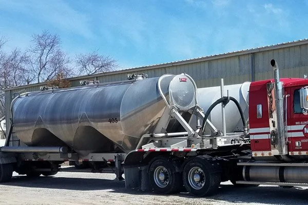 A large tanker truck parked outside near a building with a blue sky and some trees in the background.