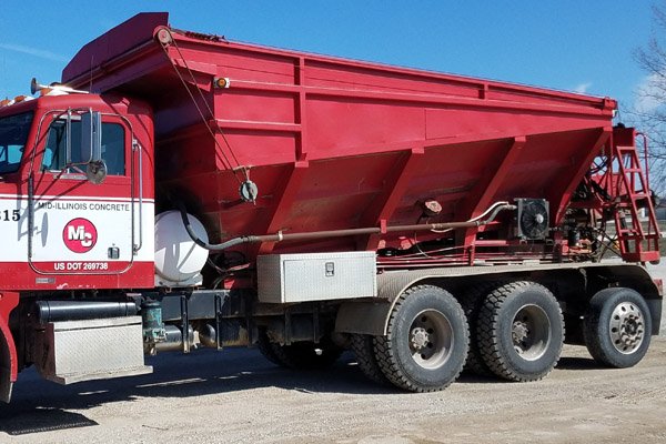 Red concrete mixer truck parked outdoors on a clear day.