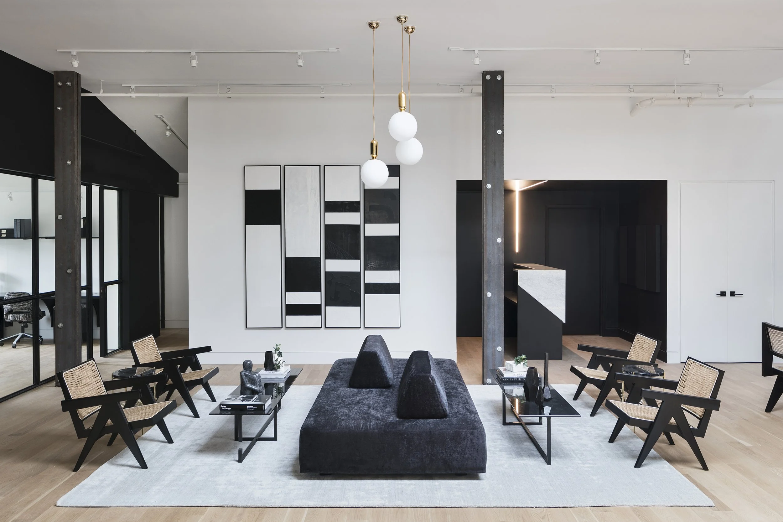 Modern living room with black and beige furniture, artwork on white wall, and pendant lighting