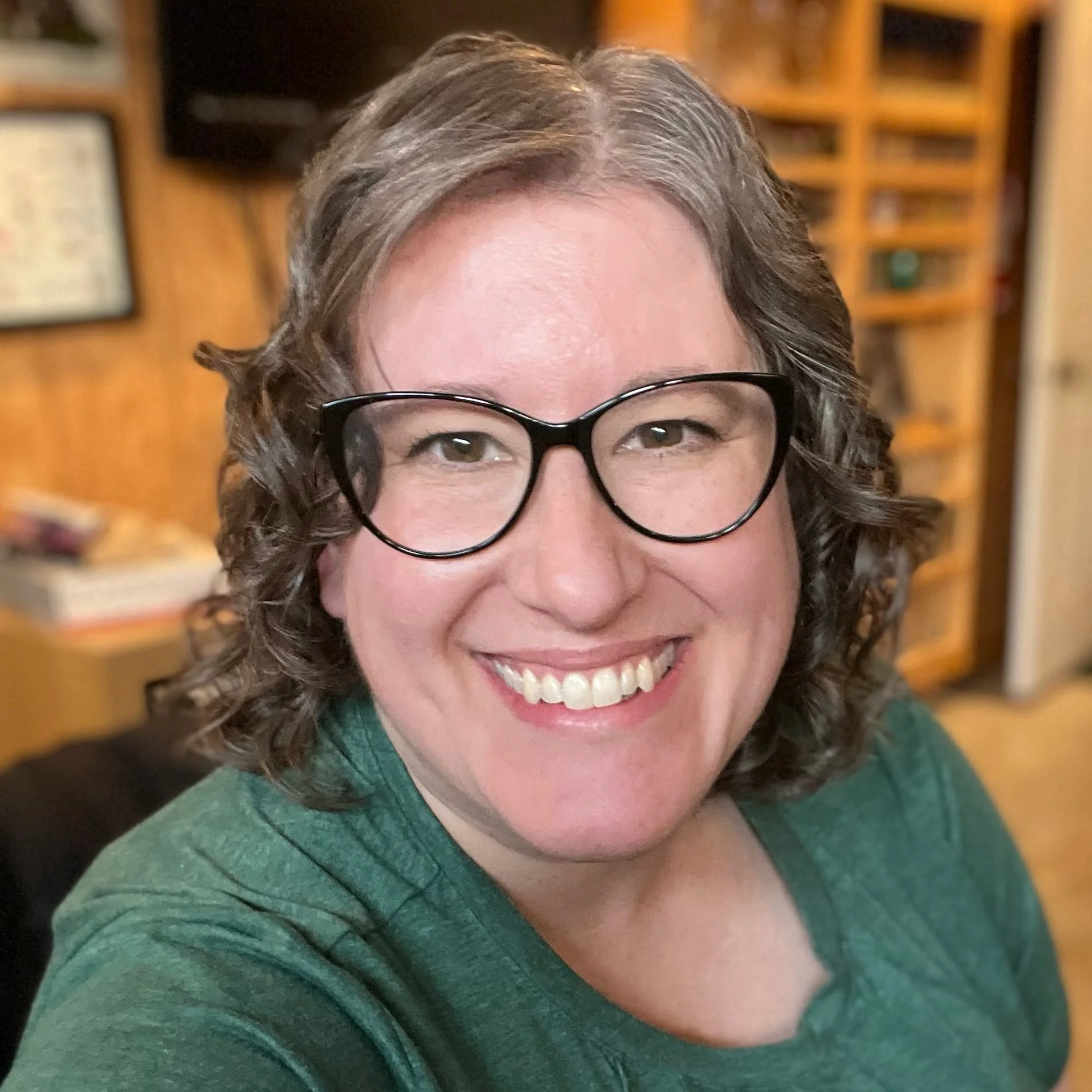 Missy wearing a green shirt, in a room with wooden shelves and framed pictures in the background.