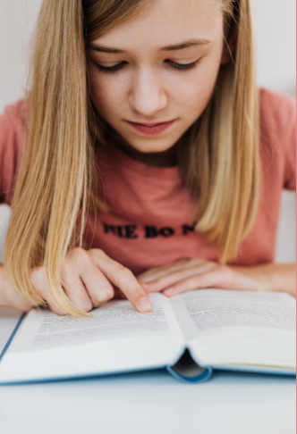 Young girl reading a book at a desk, concentrating on the pages.