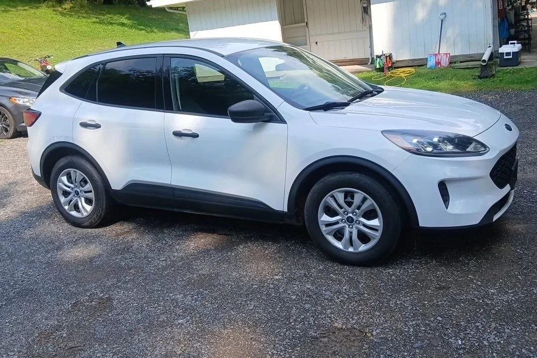 White compact SUV parked on a gravel driveway with a lawn and a shed in the background.