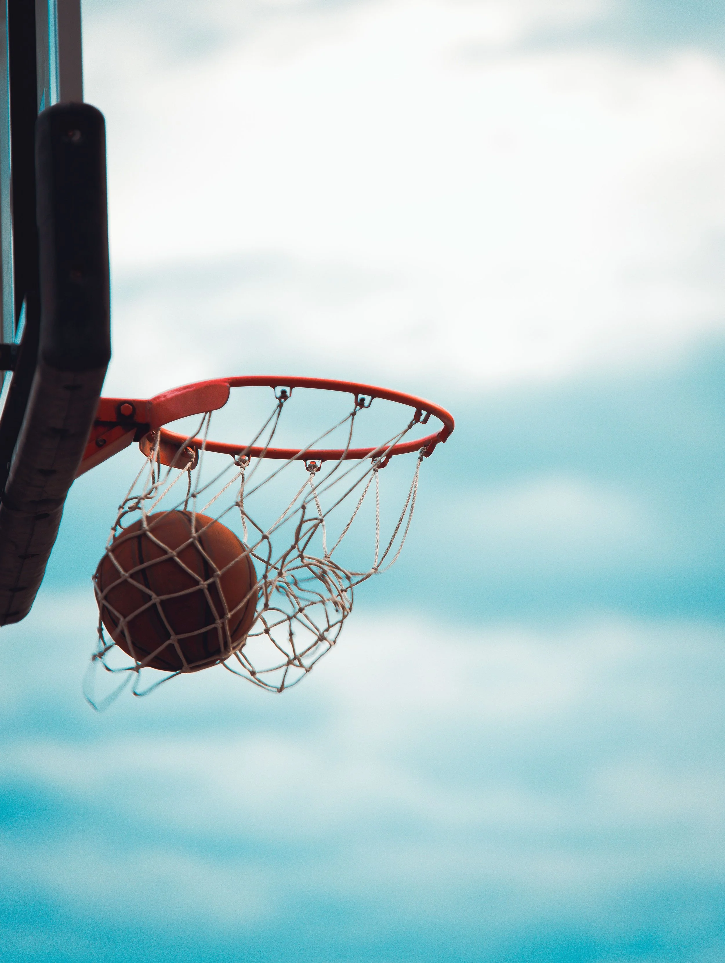 Basketball going through a hoop against a cloudy sky