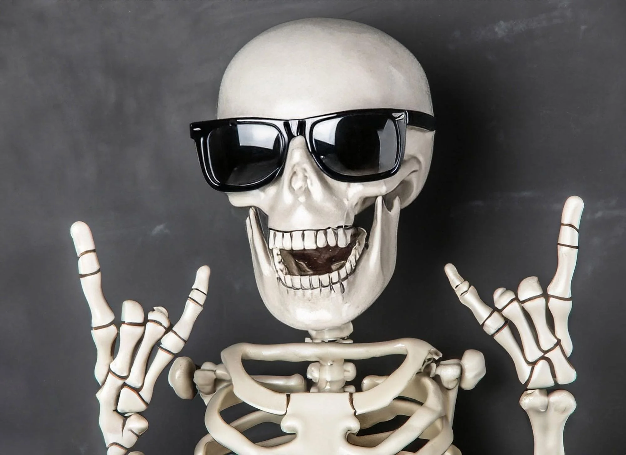 A skeleton wearing sunglasses and making a peace sign with both hands.