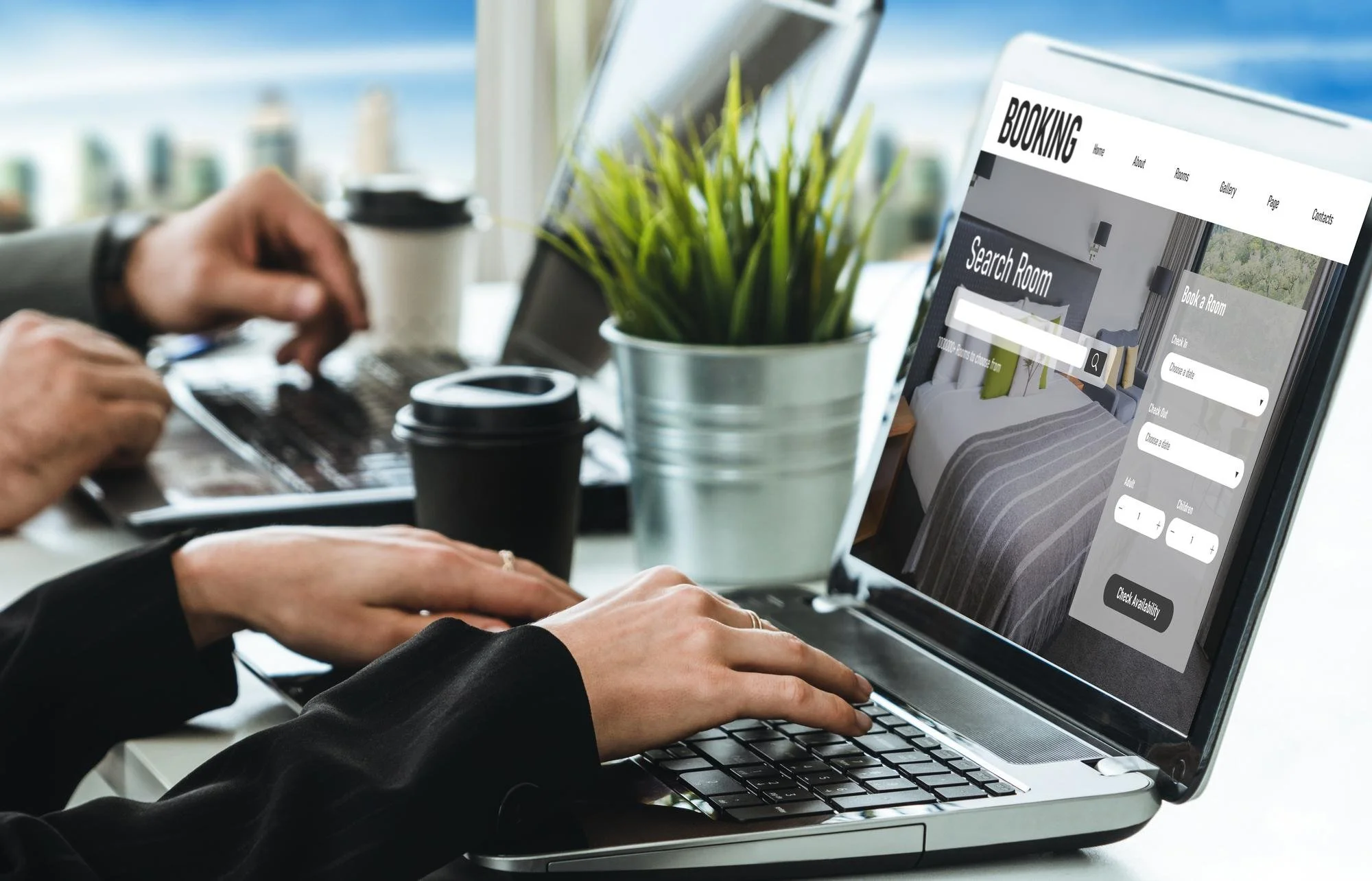 Person using a laptop at a desk with a plant and coffee cups, browsing a hotel booking website.