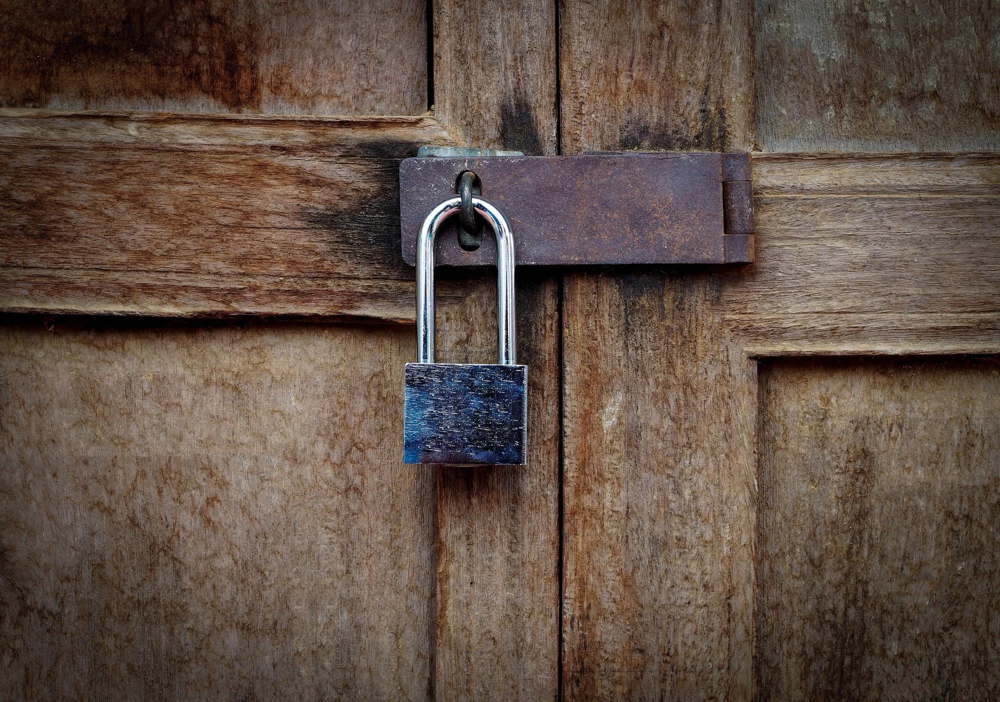 A wooden door with a rusty latch and a silver padlock securing it.