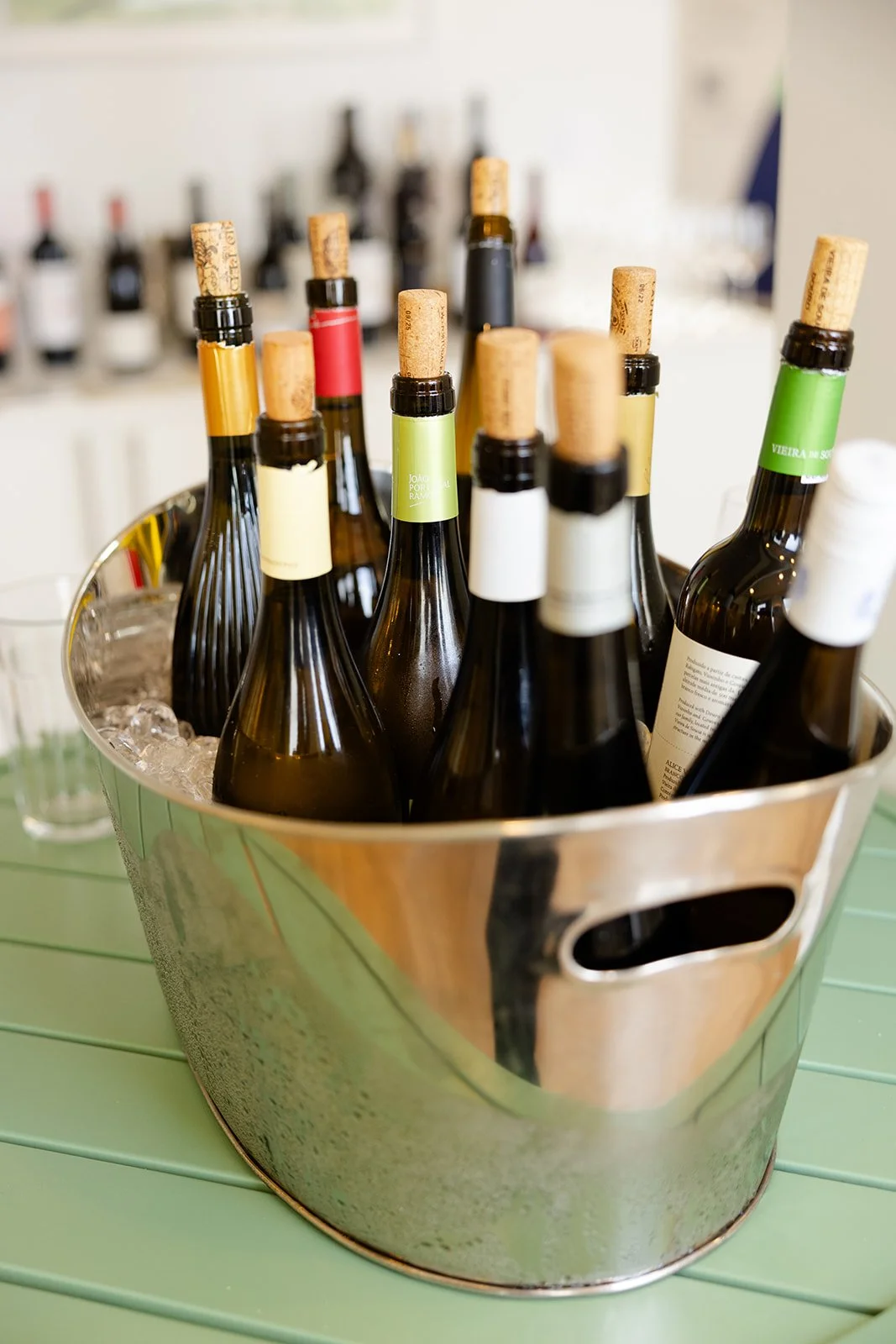 Bottles of wine in a silver ice bucket with ice, on a green table at a social gathering or event.