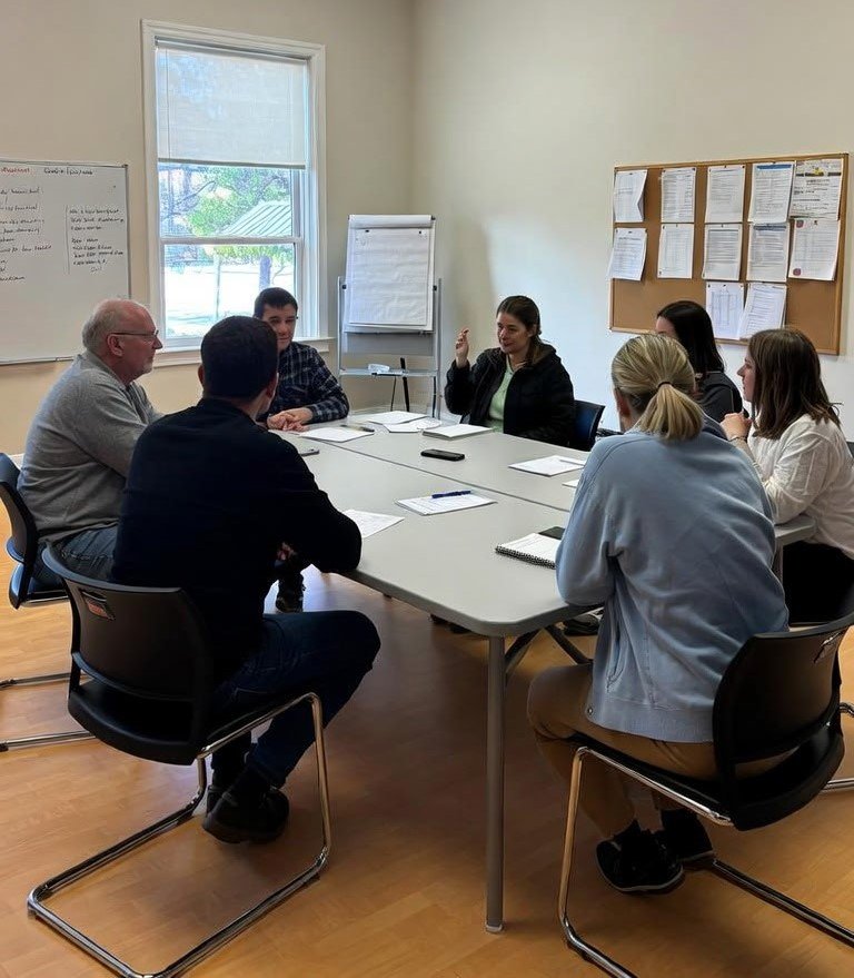A group of people sitting around a conference table in a room with papers. They are engaged in a discussion.
