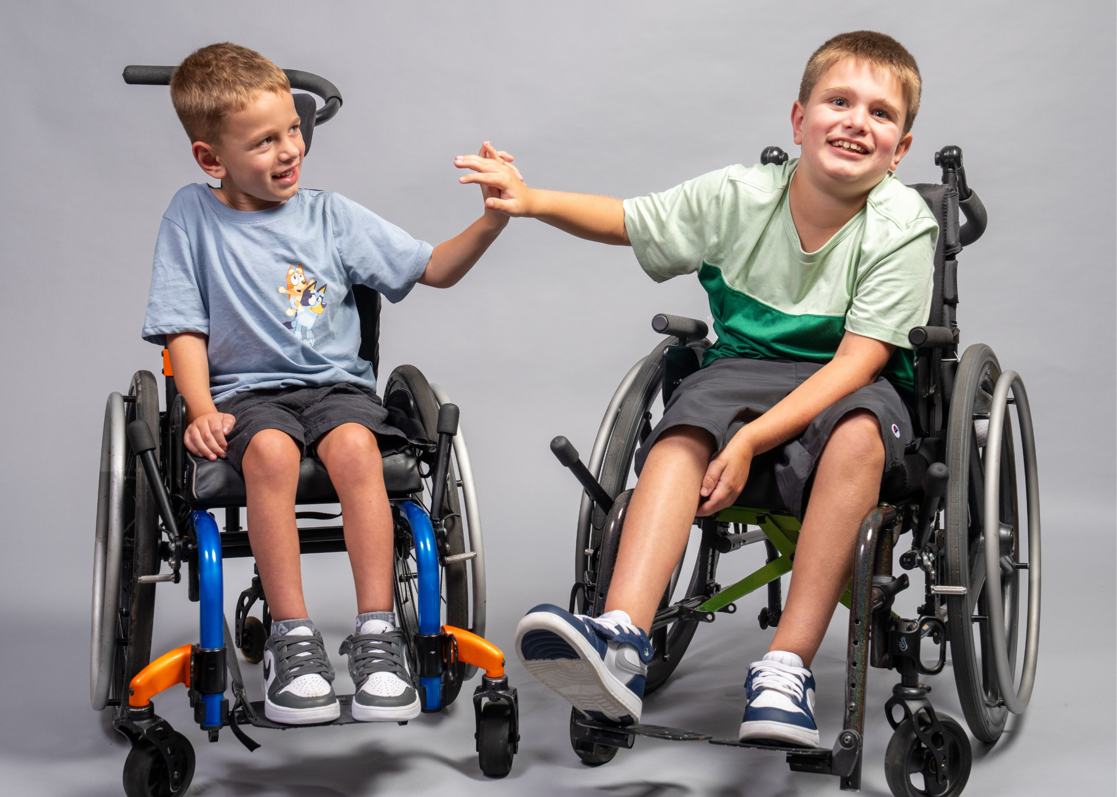 Two boys in wheelchairs high-fiving