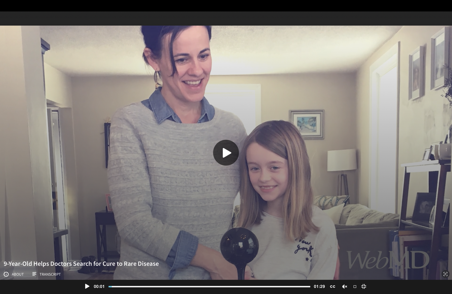 A woman and a young girl smiling and looking at an object with a black sphere in a bright living room.