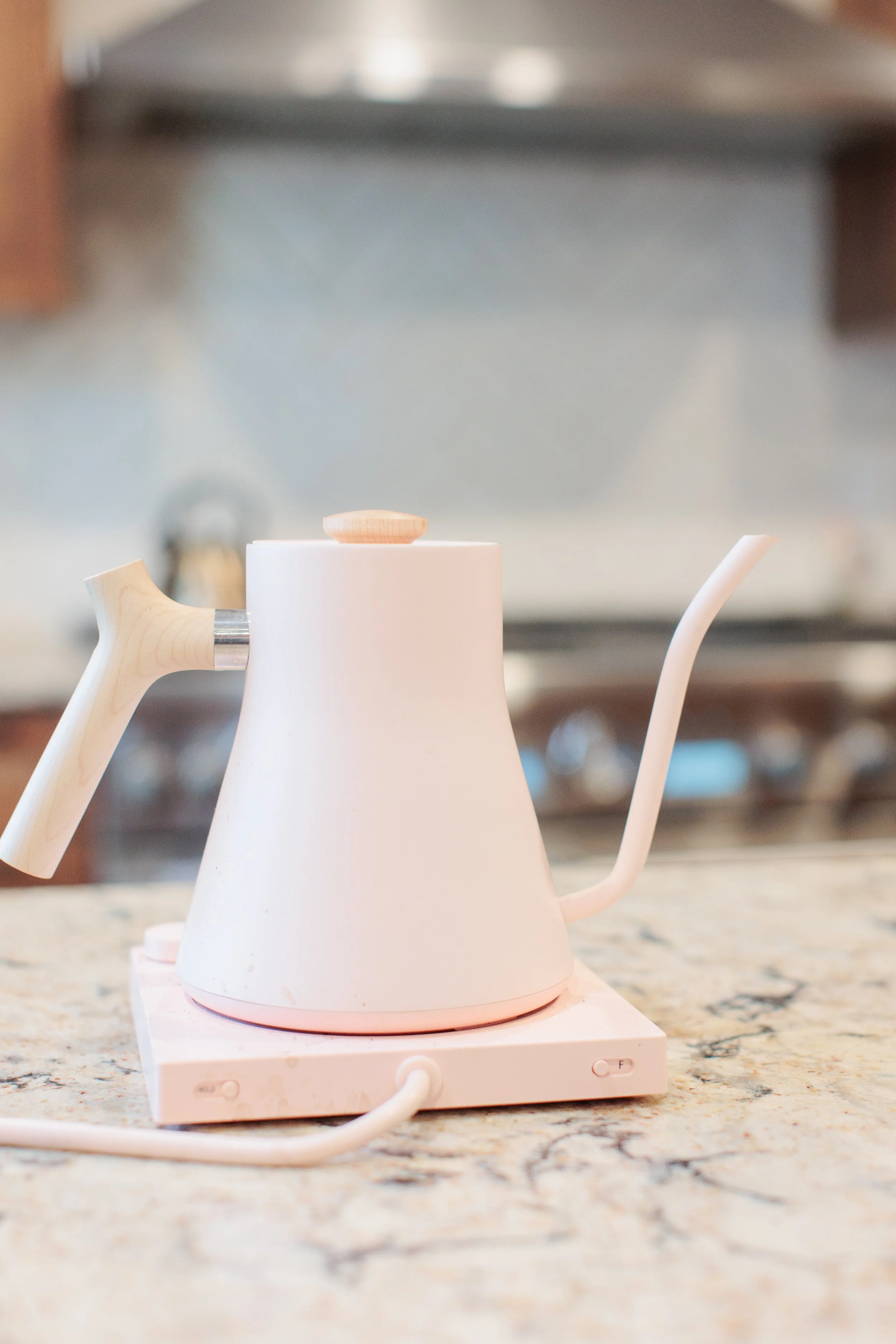 A white electric kettle on a stovetop in a kitchen with a granite countertop.