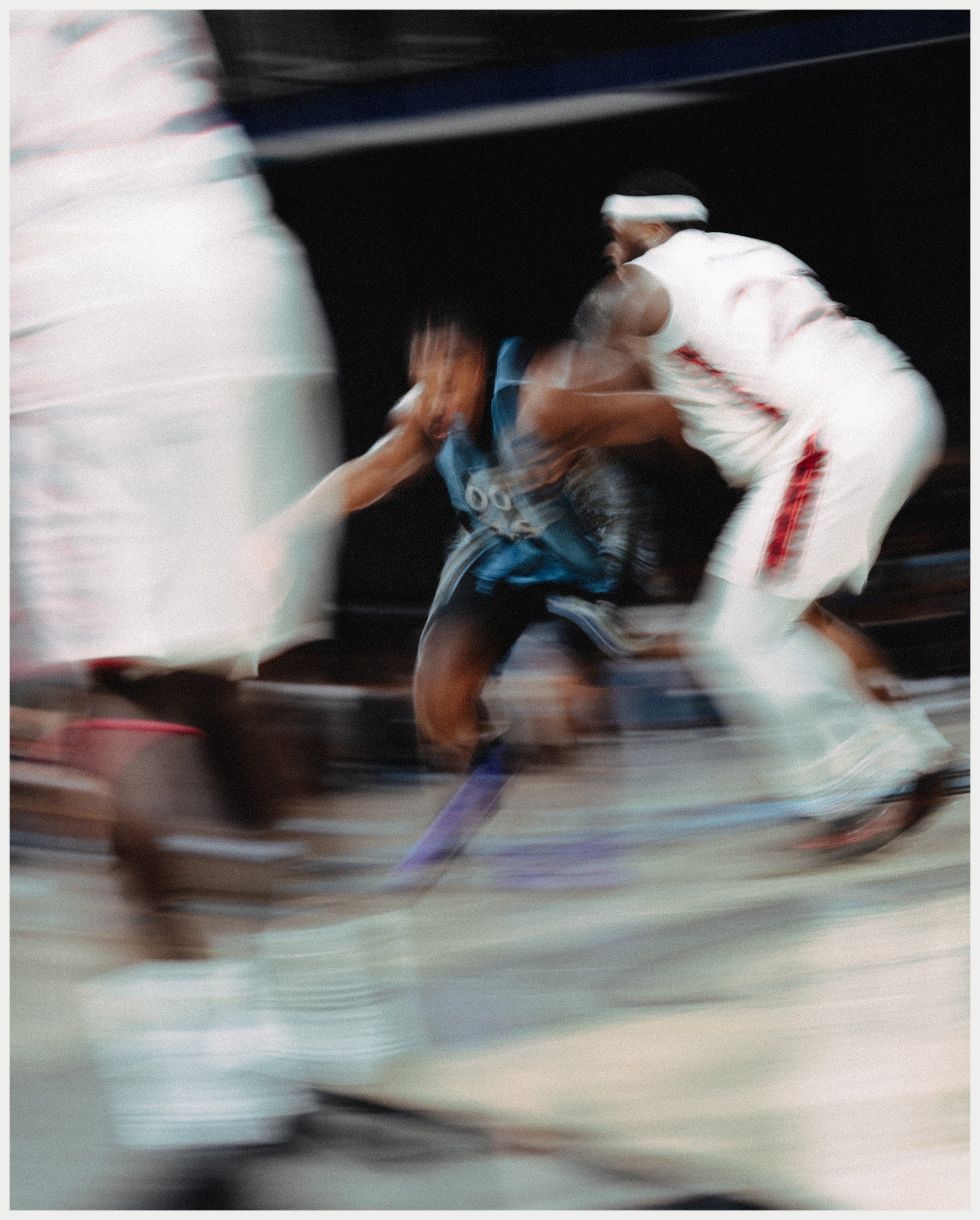 Two martial artists in white uniforms with black belts engaged in a fighting match on a dojo floor, with motion blur indicating fast movement.