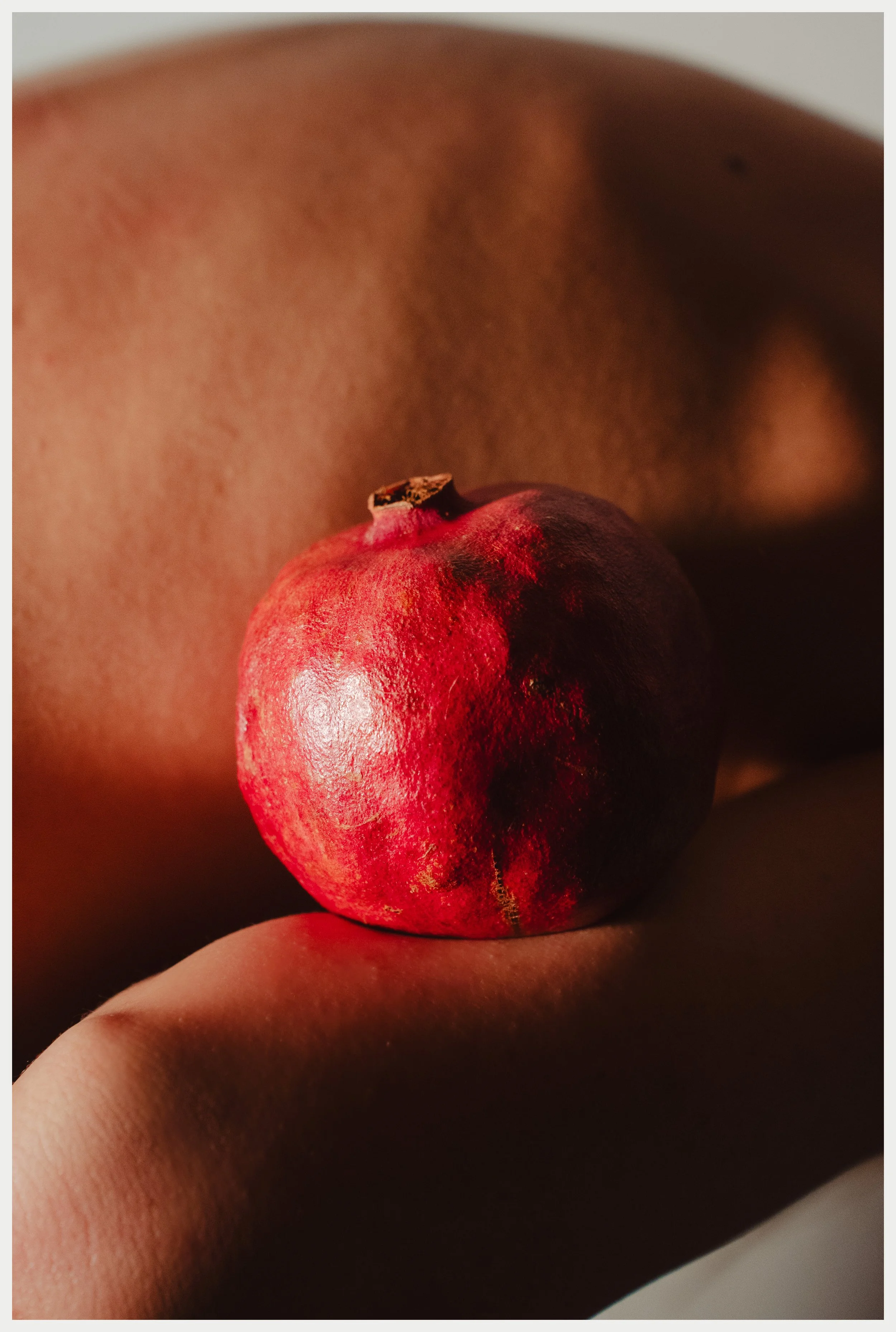 Close-up of a red pomegranate fruit being held between fingers.