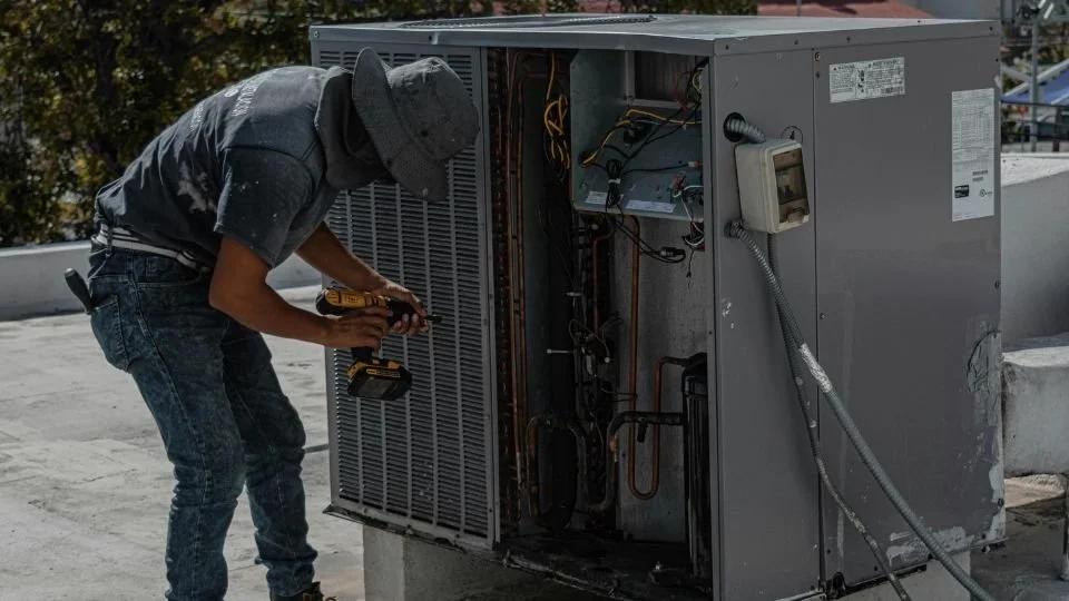 A technician working on the internal components of an air conditioning unit on a rooftop.