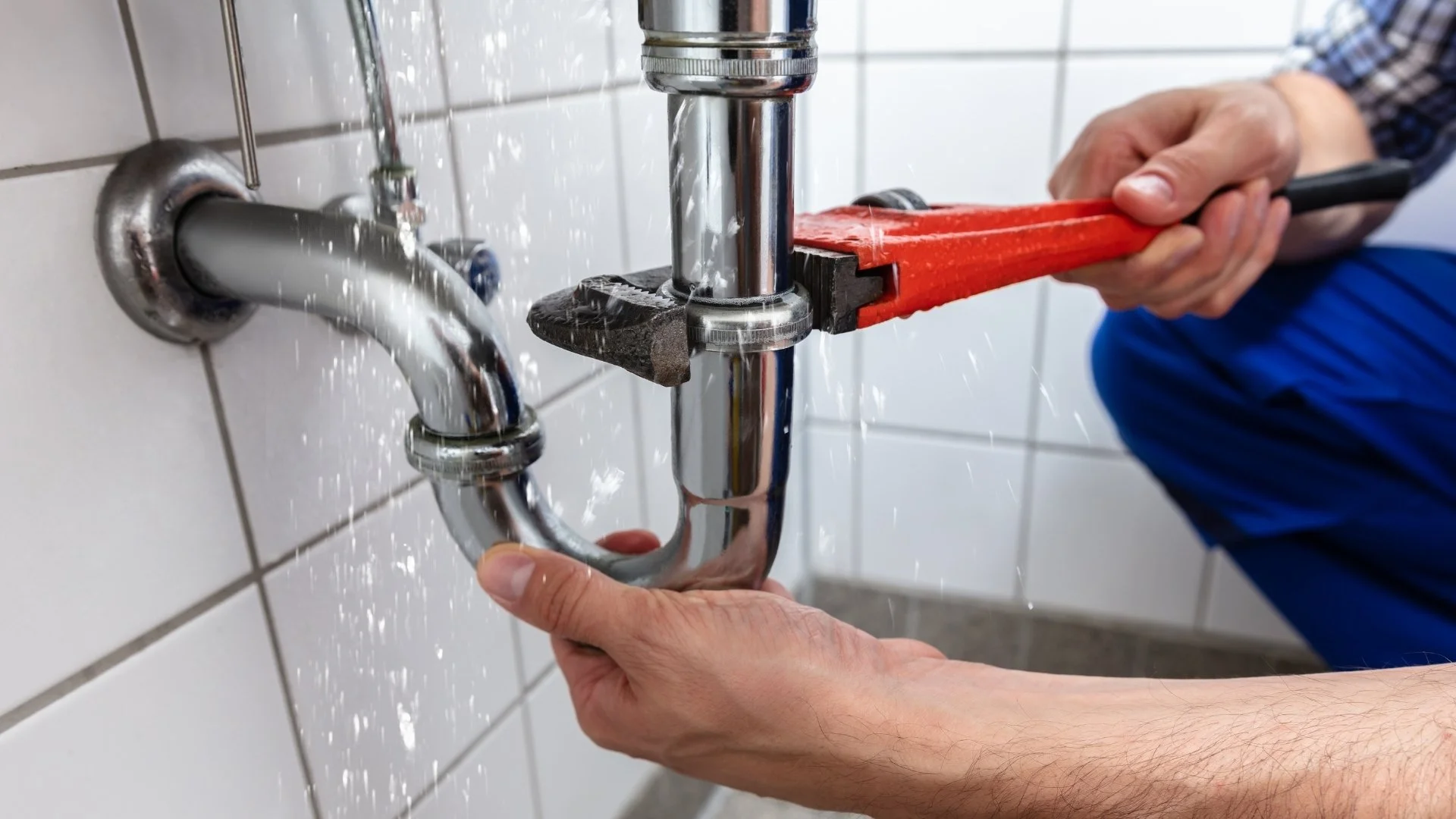 Person using a pipe wrench to tighten or loosen plumbing pipes and fittings under a sink.