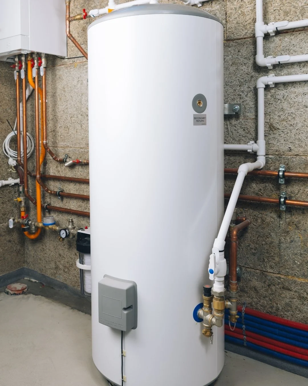 White water heater tank with plumbing and pipes next to a masonry wall.