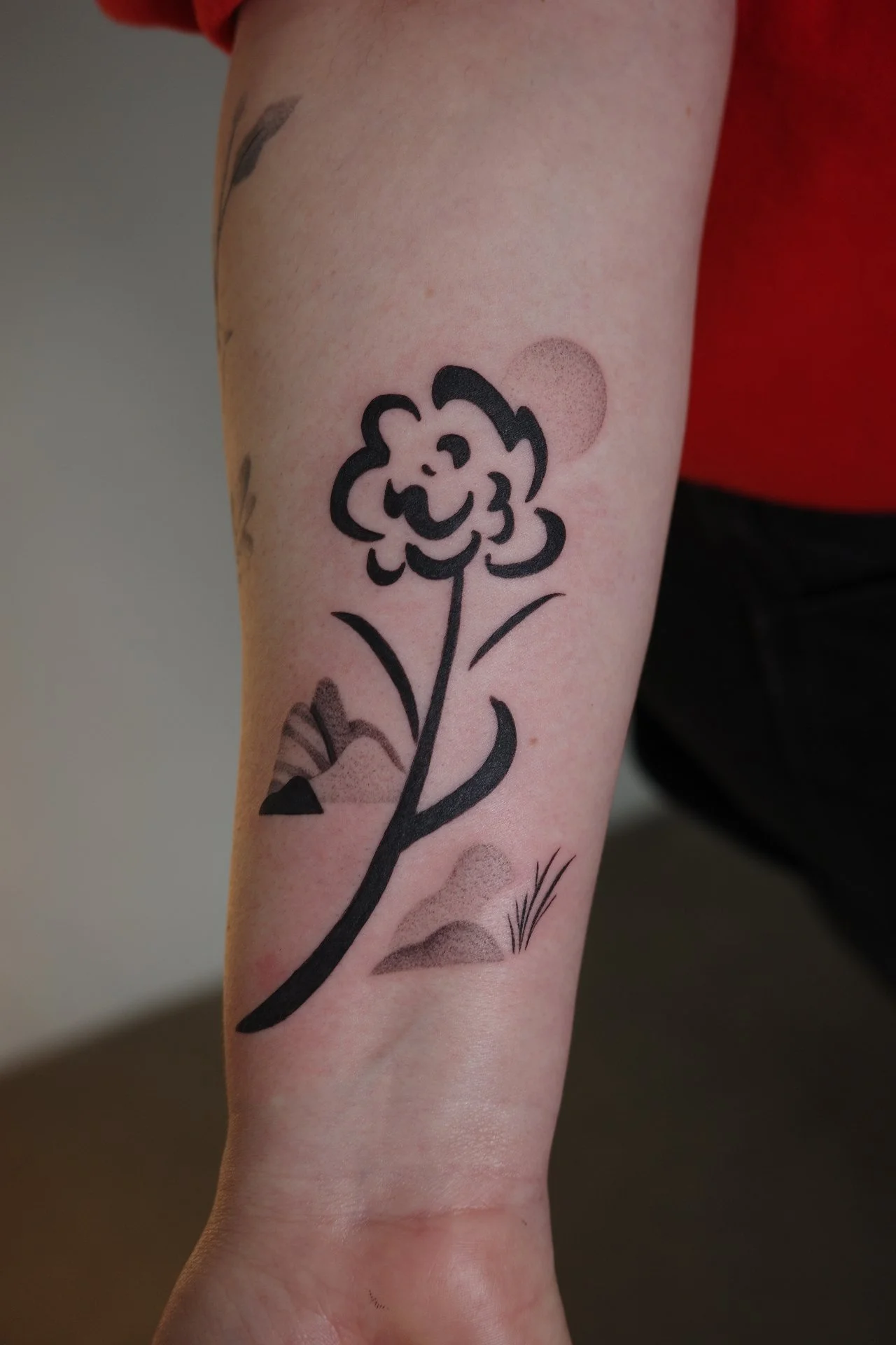 Tattoo of a smiling flower with leaves on the arm, with a background of small dots and some grass-like lines.