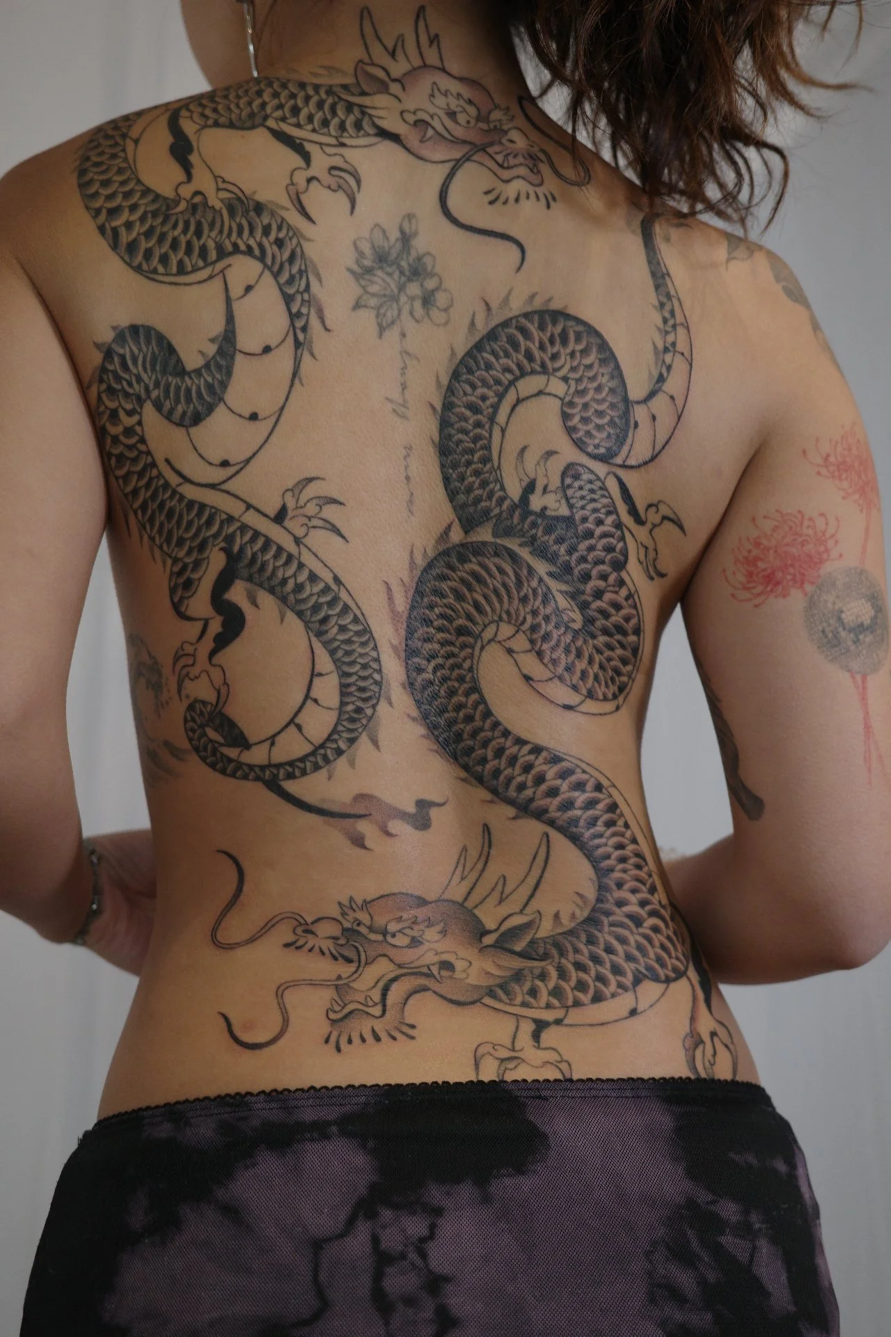 A person with a large black and gray dragon tattoo covering their chest, stomach, and side.