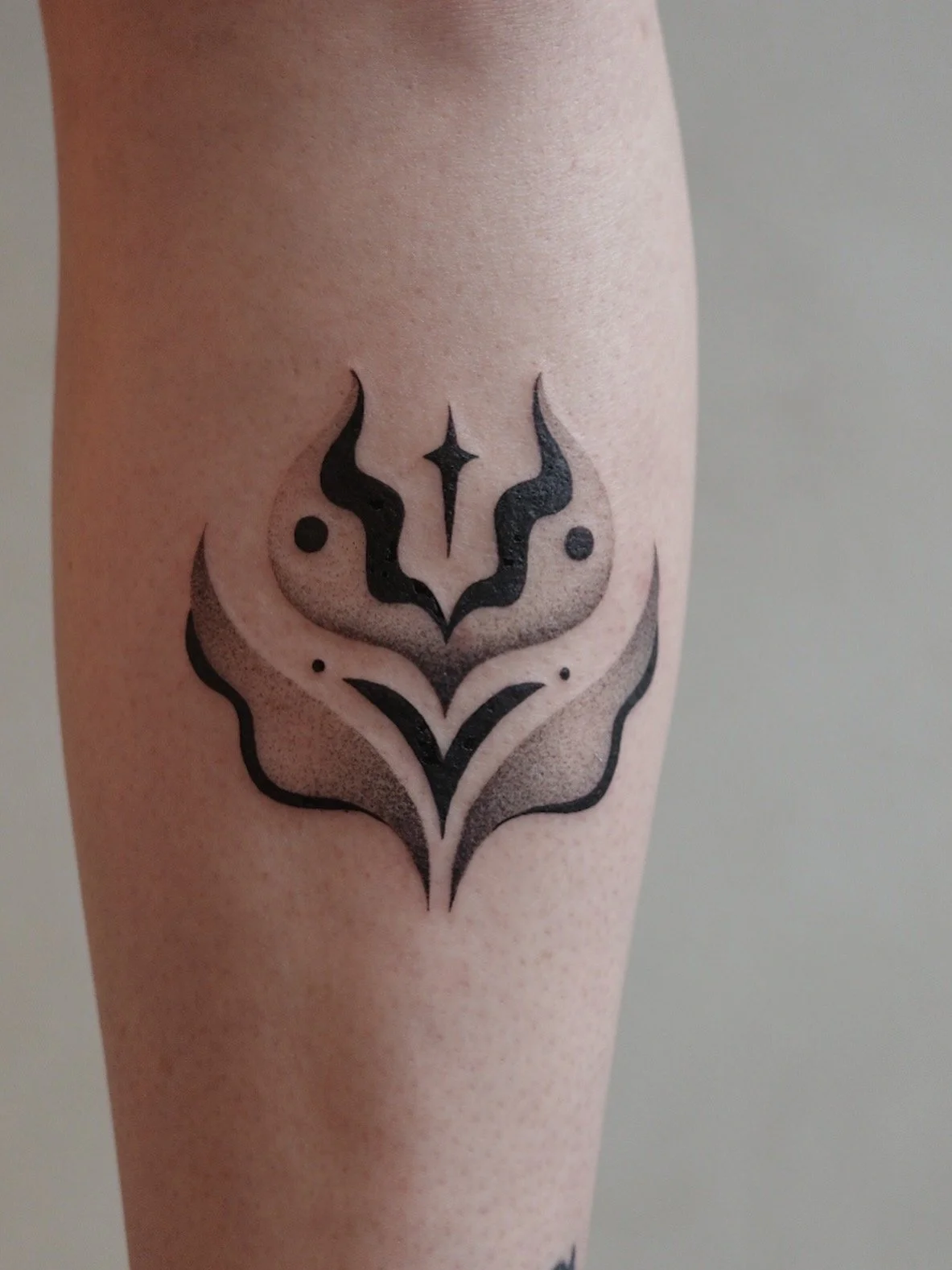 Black ink abstract geometric tattoo on person's arm featuring symmetrical arching lines, dots, and a central diamond shape.