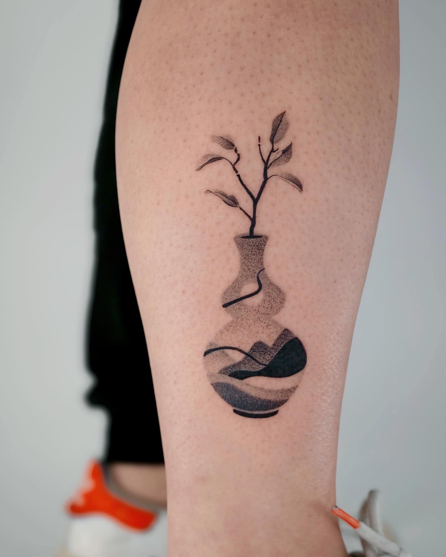 Tattoo of a houseplant in a pot with roots and a water element on a person's arm.