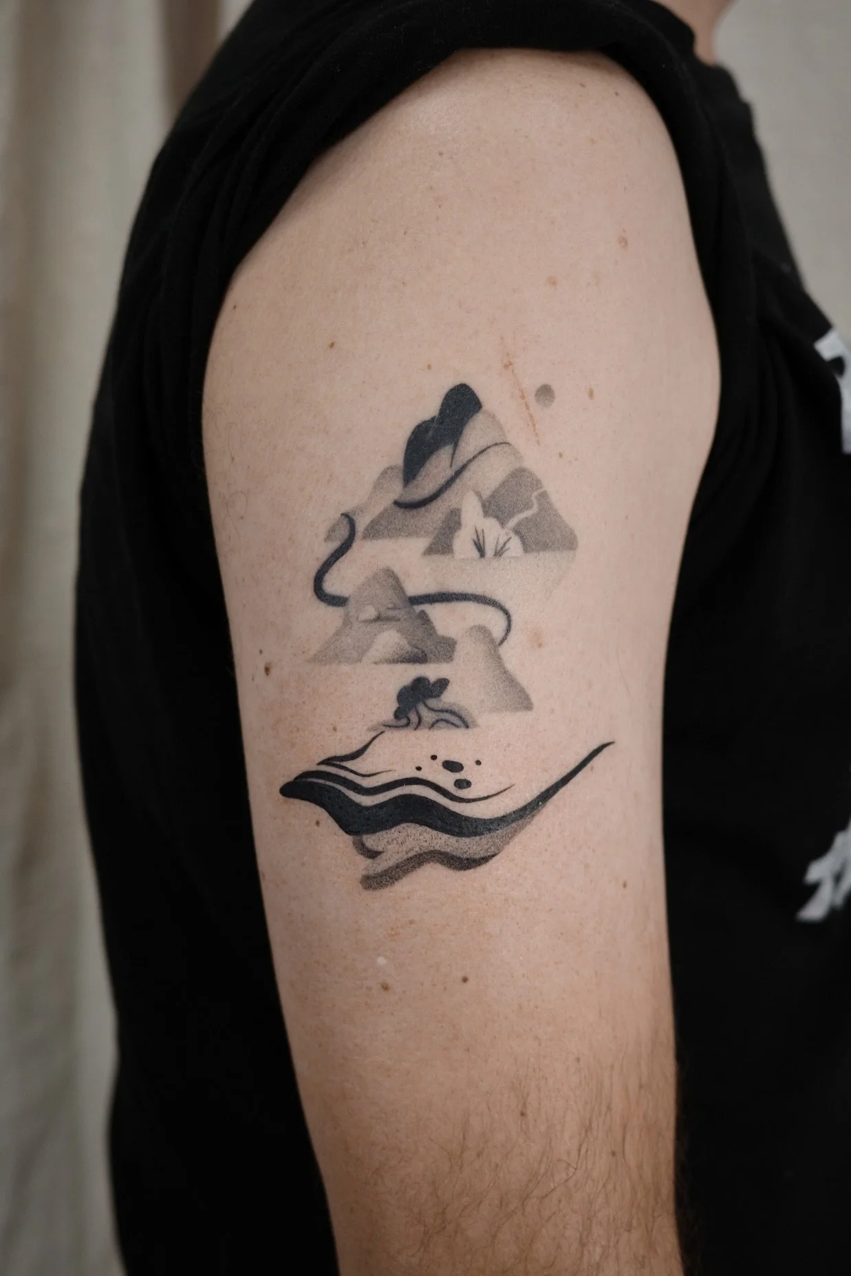Tattoo on person's upper arm of a mountain landscape with a tent, a campfire, and stylized water or land at the bottom.