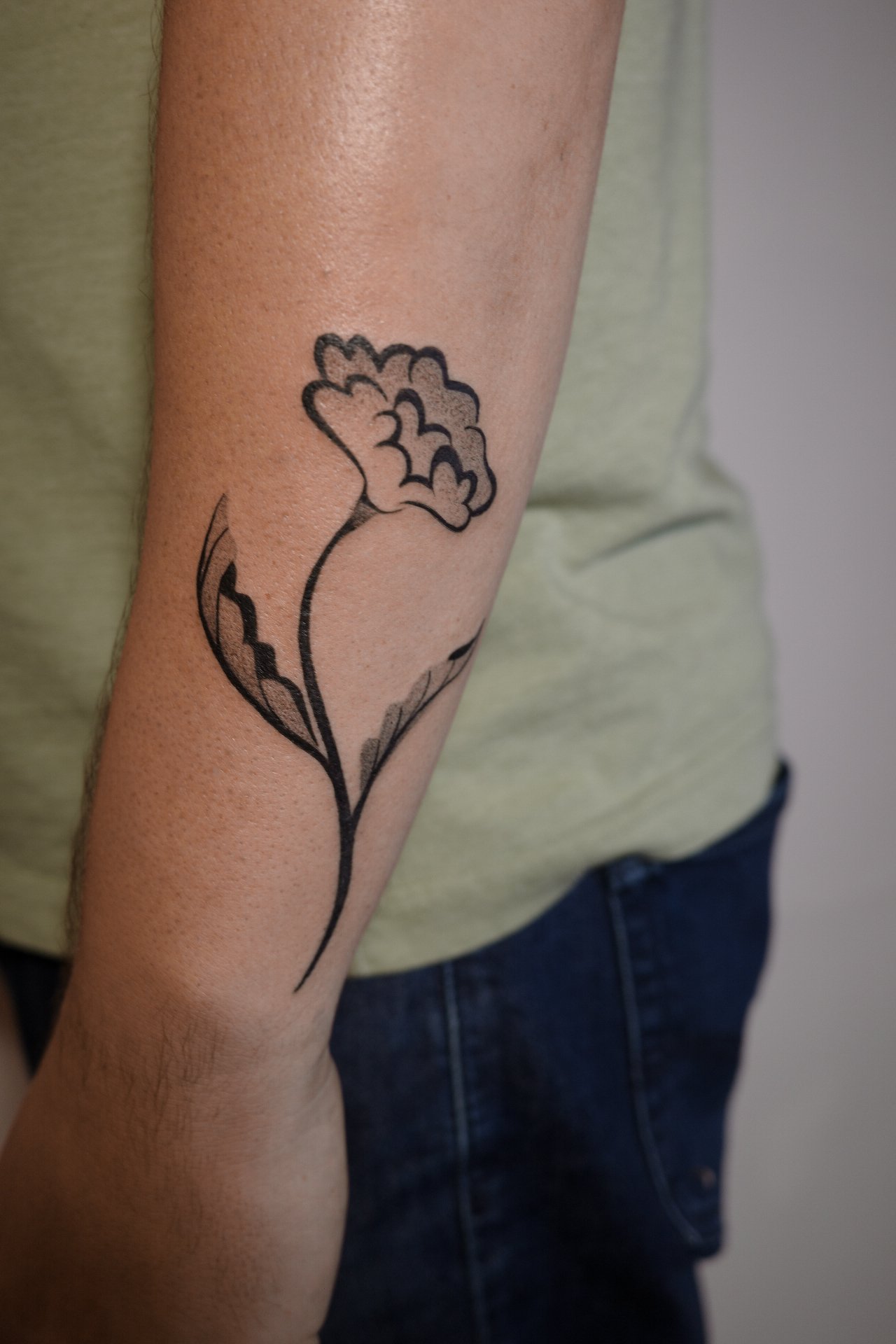 Tattoo of a flower on a person's arm, with a simple, black outline design.
