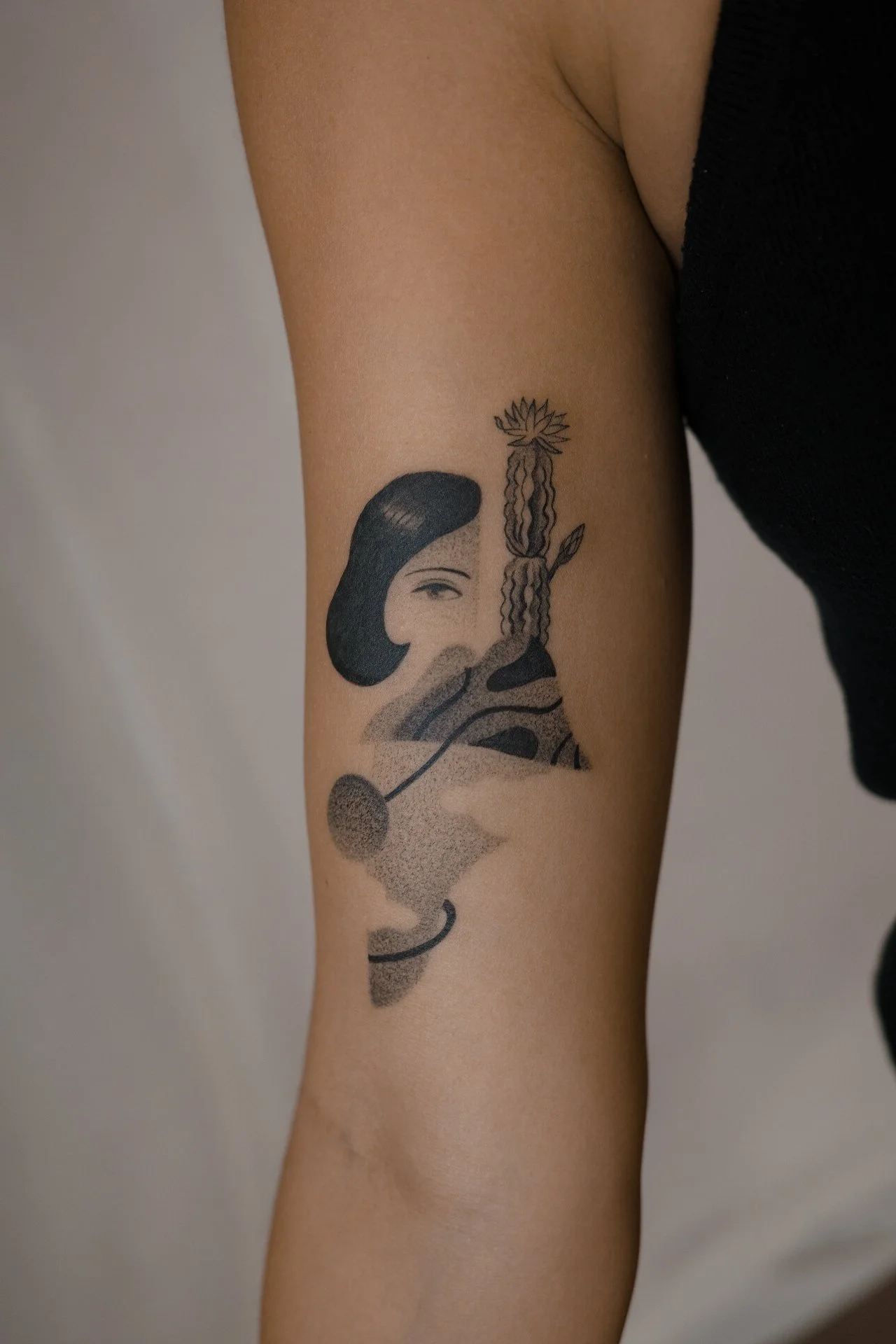 Tattoo of a woman's face with dark hair, with abstract and geometric elements, on person's arm.