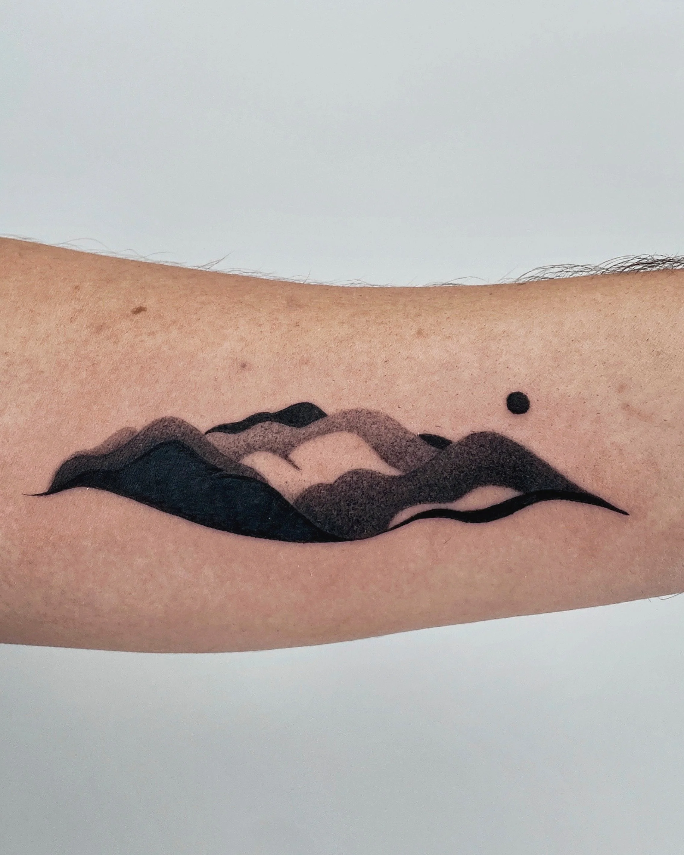 Close-up photo of a skin tattoo with black ink wavey lines and black dots on skin with some hair.