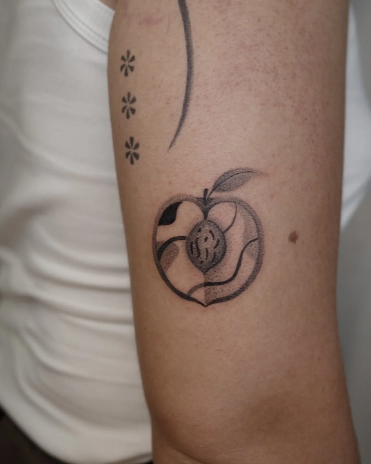 Tattoo of a smiling face inside a heart shape on a person's upper arm, with small floral designs nearby.
