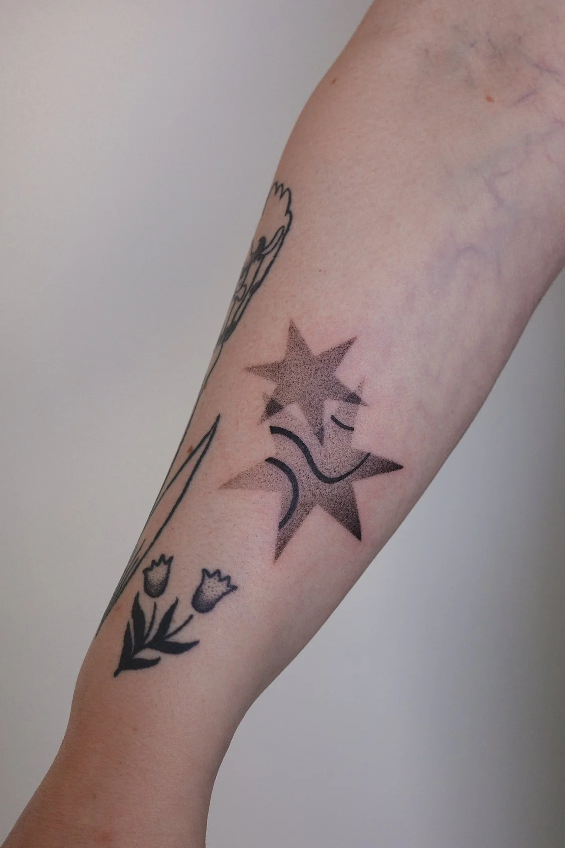Tattooed arm with two black stars and a small smiley face among other tattoos. The stars have a gradient shading.